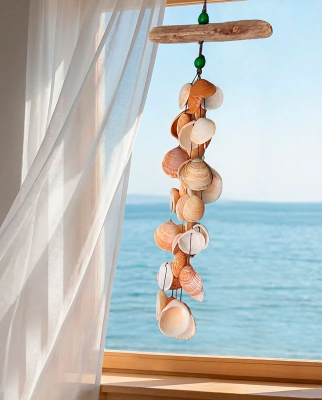 ananushu-piezas-deco-marina Deco marina con colgante de conchas suspendido frente a una ventana con vistas al mar.