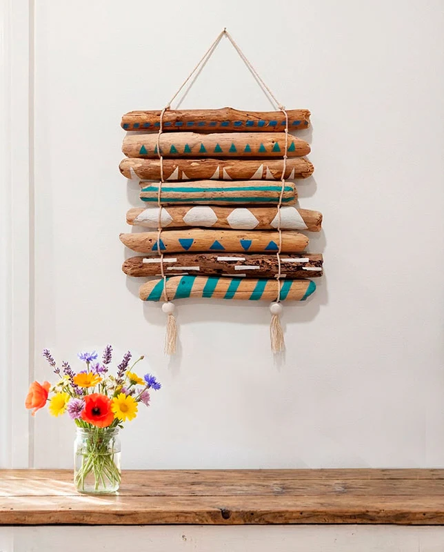 arte-madera-driftwood Tapiz de pared rústico hecho con troncos de madera varada y pintura geométrica azul y blanca.