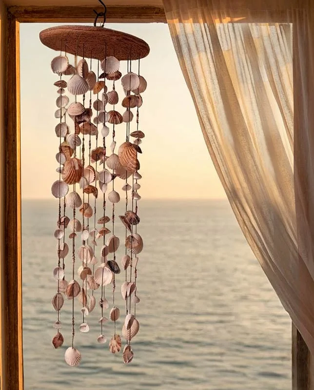 Gran móvil de conchas circular colgado frente a una ventana al mar.