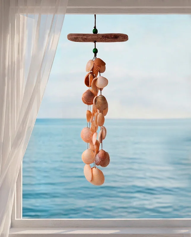 Colgante de conchas con cuentas verdes y madera marina sobre una ventana al mar.