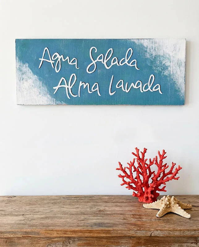 Cuadro artesanal azul claro con la frase "Agua salada, alma lavada" pintado a mano.