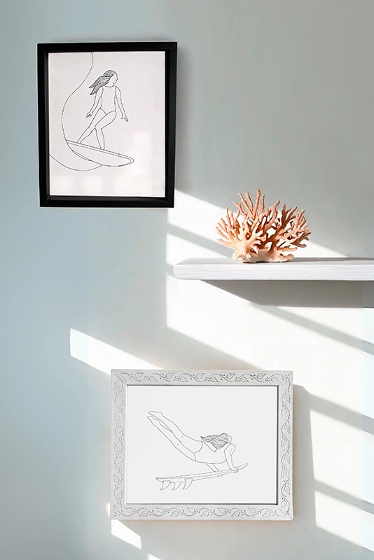 Ambiente de pared con dos láminas enmarcadas de ilustraciones de surf lineales y un coral decorativo.