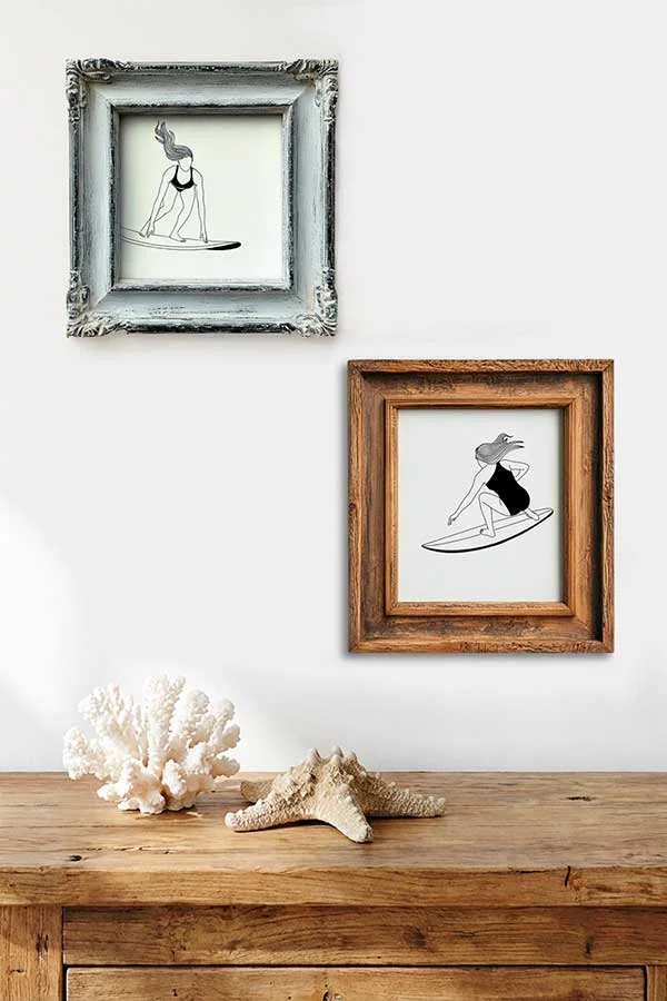 Ambiente de pared con dos láminas enmarcadas de ilustraciones de surf lineales y un coral decorativo.