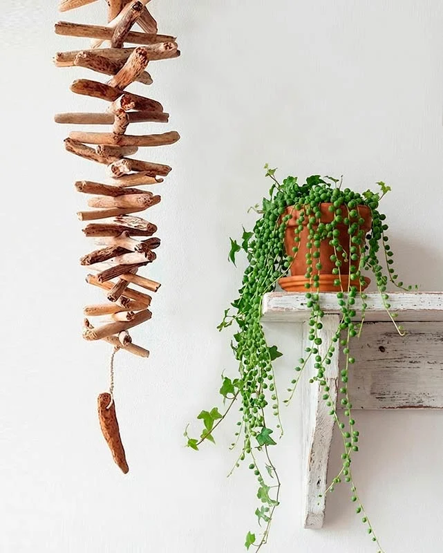 Guirnalda colgante vertical hecha con pequeños troncos de madera varada en forma de cascada.