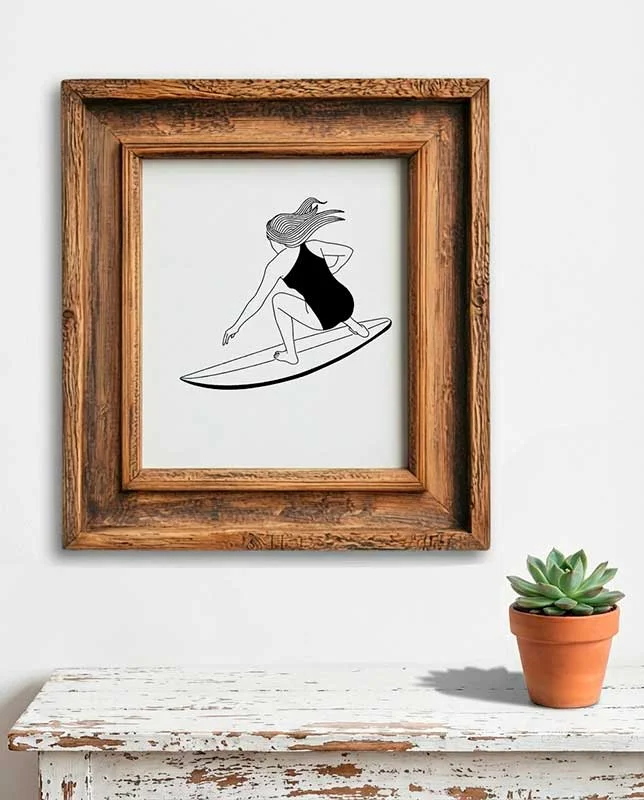 Lámina enmarcada de mujer haciendo surf en trazo negro minimalista.