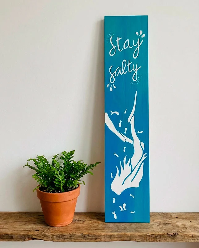 letrero-madera-decorativo-costero Letrero de madera turquesa con la frase pintada a mano "Stay Salty" y una ilustración de una buceadora en blanco.