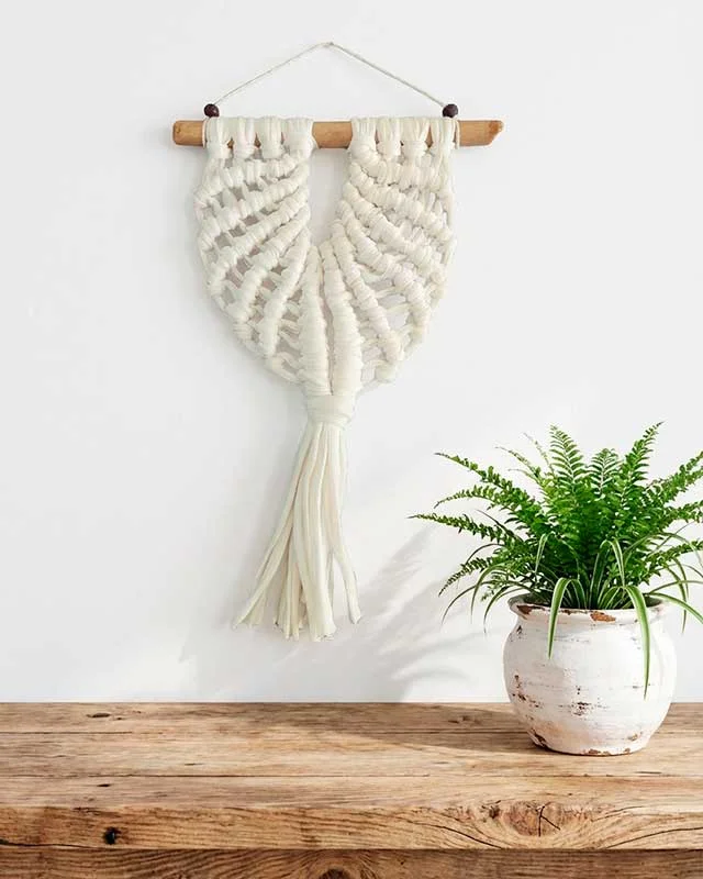 Macramé decorativo blanco con forma de concha marina y fleco central.