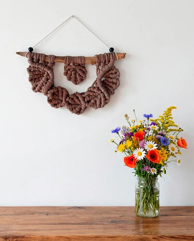 Macramé pequeño con hojas tejidas en color marrón suave sobre madera.