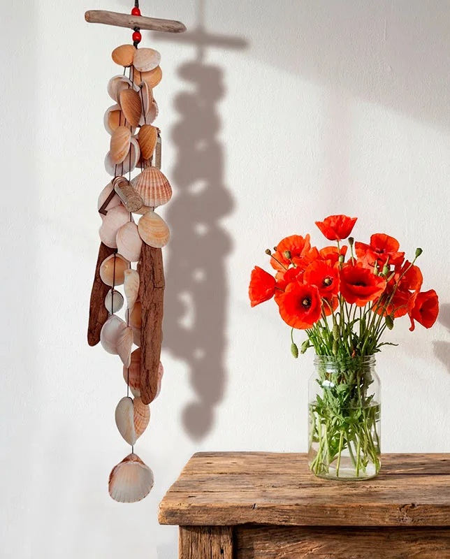 Móvil de conchas y madera varada (driftwood) con sombras en la pared.