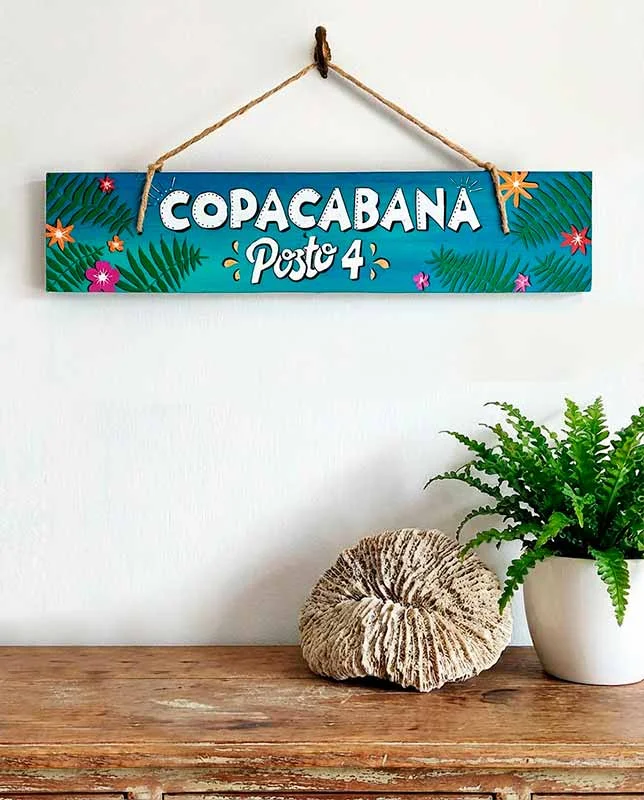 Letrero de madera pintado a mano "Copacabana" con hojas tropicales.