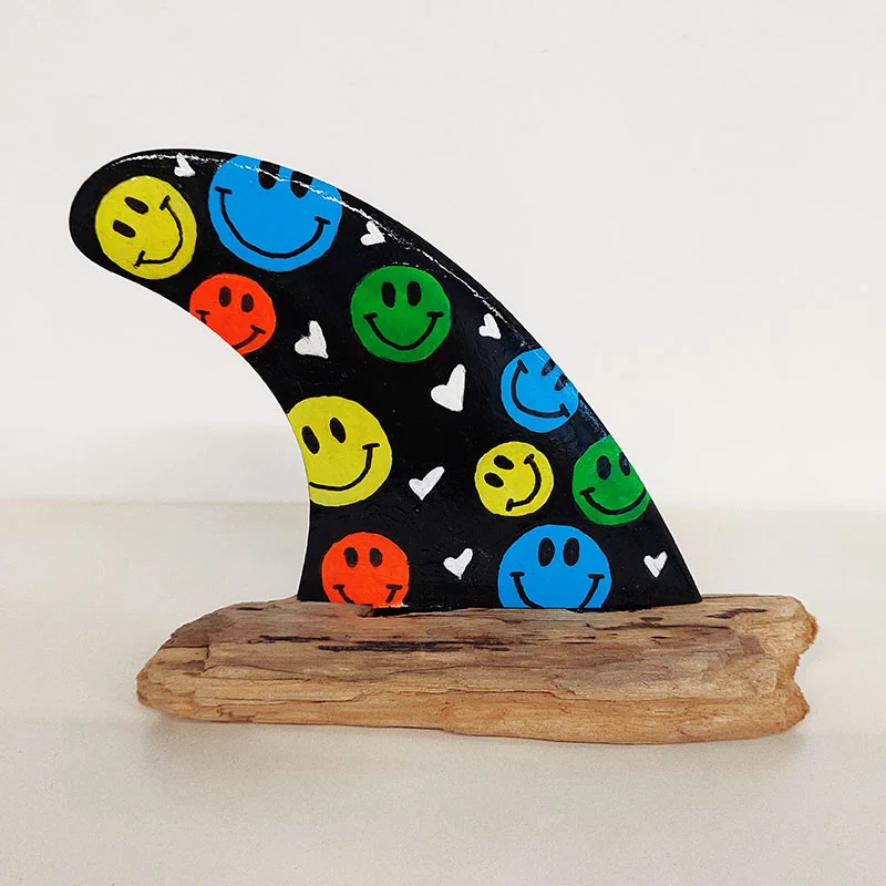 Quilla amarilla con la icónica cara sonriente (smiley) sobre madera.