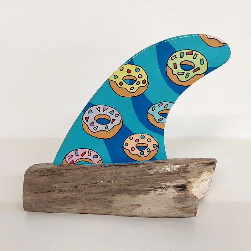 Quilla de surf azul vibrante con patrón de donuts de colores sobre madera.