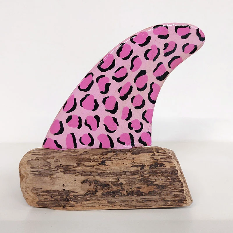Quilla de surf con patrón de piel de pantera rosa y manchas artesanales sobre madera.