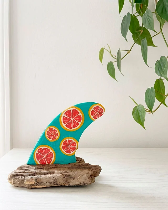 quilla-surf-pintada-acrilico Una quilla de tabla de surf decorativa de color turquesa intenso con estampados de rodajas de pomelo rosado.