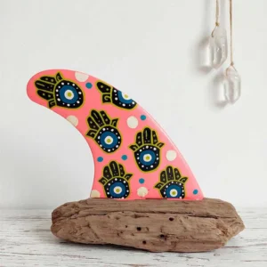 Quilla decorativa en rosa chicle con estampado de manos de hamsa y ojos protectores estilo turco en azul y amarillo sobre madera de deriva.